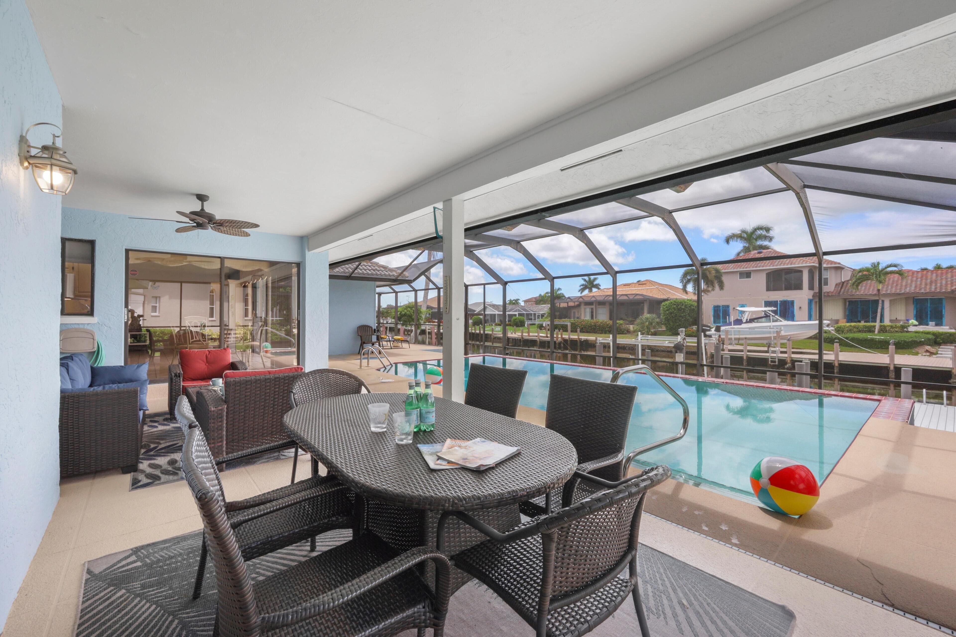 A covered outdoor area with a pool, wicker furniture, and a view of neighboring buildings.