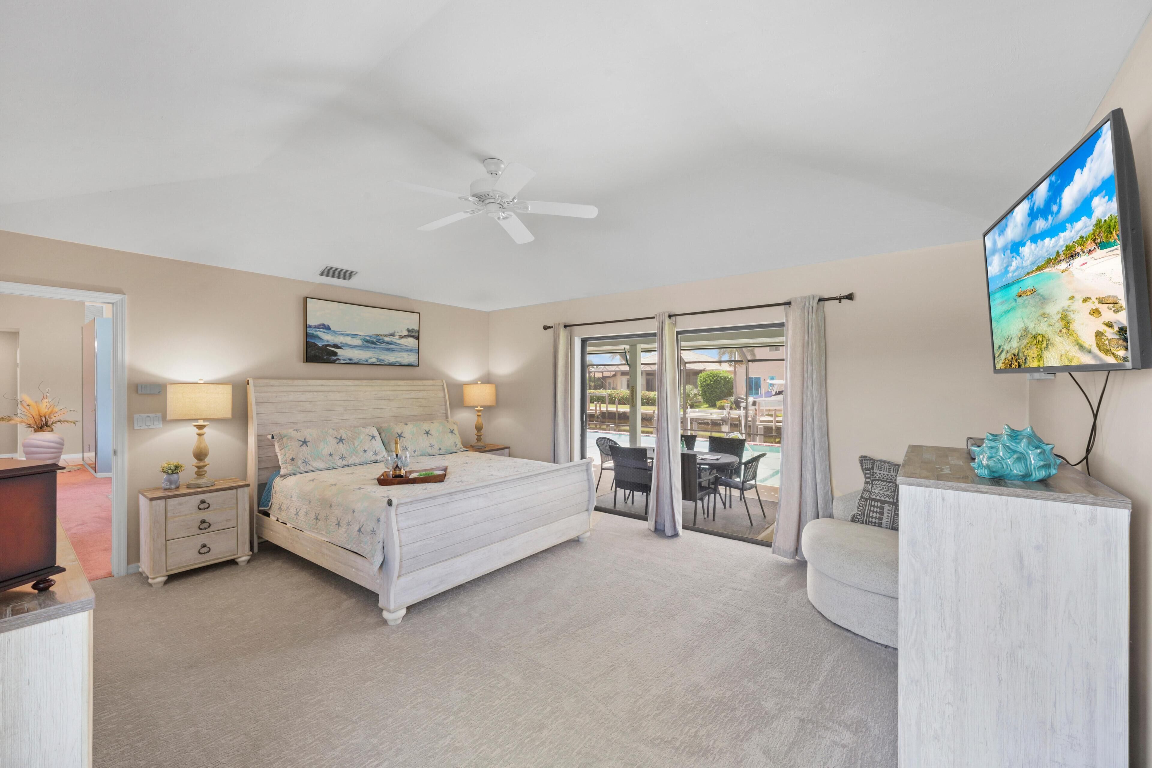 A bedroom with a bed, bedside tables, a ceiling fan, a TV, and a view of the outdoors through a sliding door.