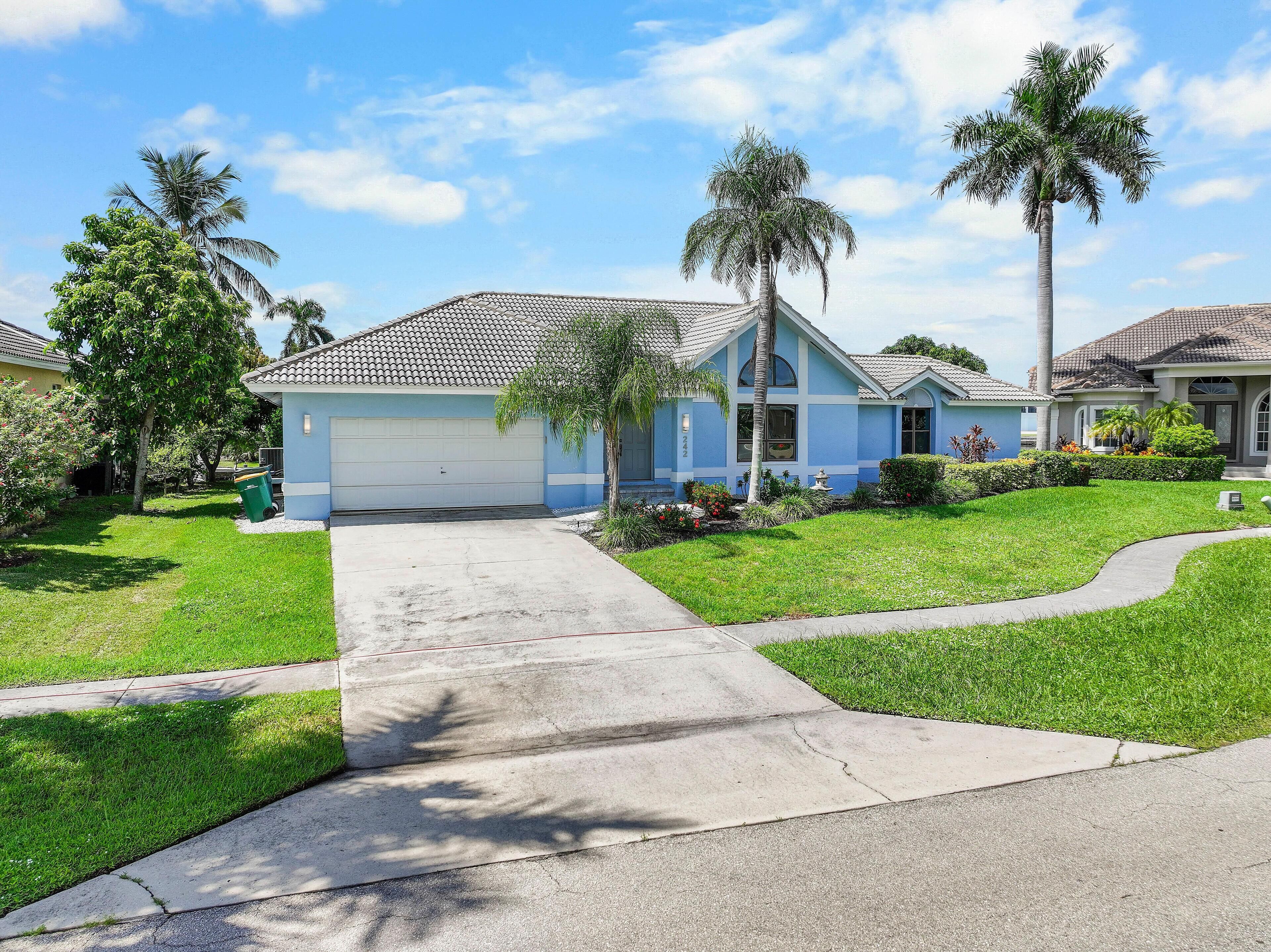 A residential house with a garage, a well-maintained lawn, and palm trees.