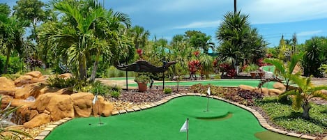 Ein Minigolfplatz mit einem grünen Putting-Bereich, Sandfängen und einem dekorativen Pavillon.