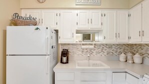 A kitchen with white cabinets, a refrigerator, a coffee maker, and a sink. - Southwinds B-2 (Marco Island)
