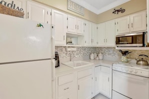 A kitchen with white cabinets, a microwave, a stove, and a tiled backsplash.