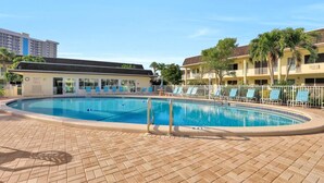 A pool area with a tiled deck, lounge chairs, and a building with a flat roof. - Southwinds B-2 (Marco Island)