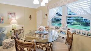 A dining area with a glass table surrounded by wicker chairs, a lamp, and artwork on the walls. - Southwinds B-2 (Marco Island)