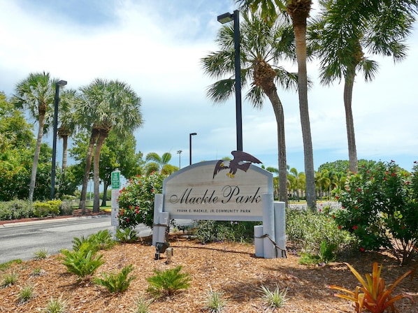 A sign for Mackle Park with an eagle emblem, surrounded by palm trees and landscaped gardens.