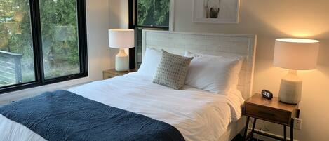 A neatly made bed with a blue blanket, two bedside lamps, a clock, and a framed picture on the wall.