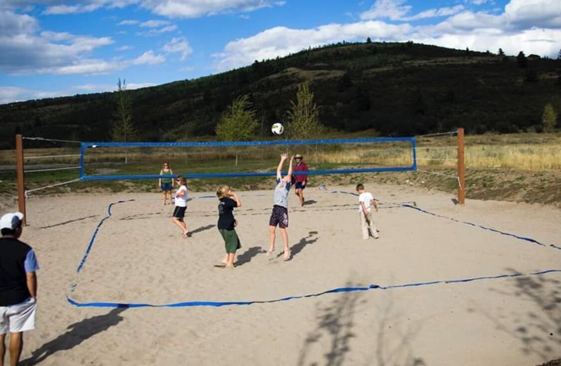 A volleyball game on a sandy court with a net, surrounded by a natural landscape.