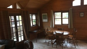 A wooden interior with a round dining table surrounded by chairs, a bench, and a leather sofa. - Shrew Lodge Hot Tub (Carmarthen)