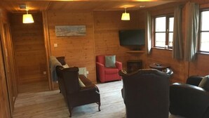 A wooden interior with a sofa, armchair, and red chair. A flat-screen TV is mounted on the wall. - Shrew Lodge Hot Tub (Carmarthen)
