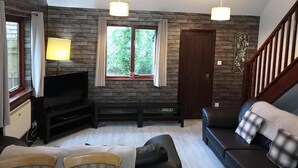 A living room with a TV, sofa, and chairs, wooden walls, and a staircase. - Primrose 20 Hot Tub (Carmarthen)