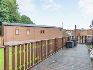 A wooden cabin with two windows and a metal roof, surrounded by a wooden deck and a fence. - Woodlands - Bridlington Links (Sewerby, near Bridlington)