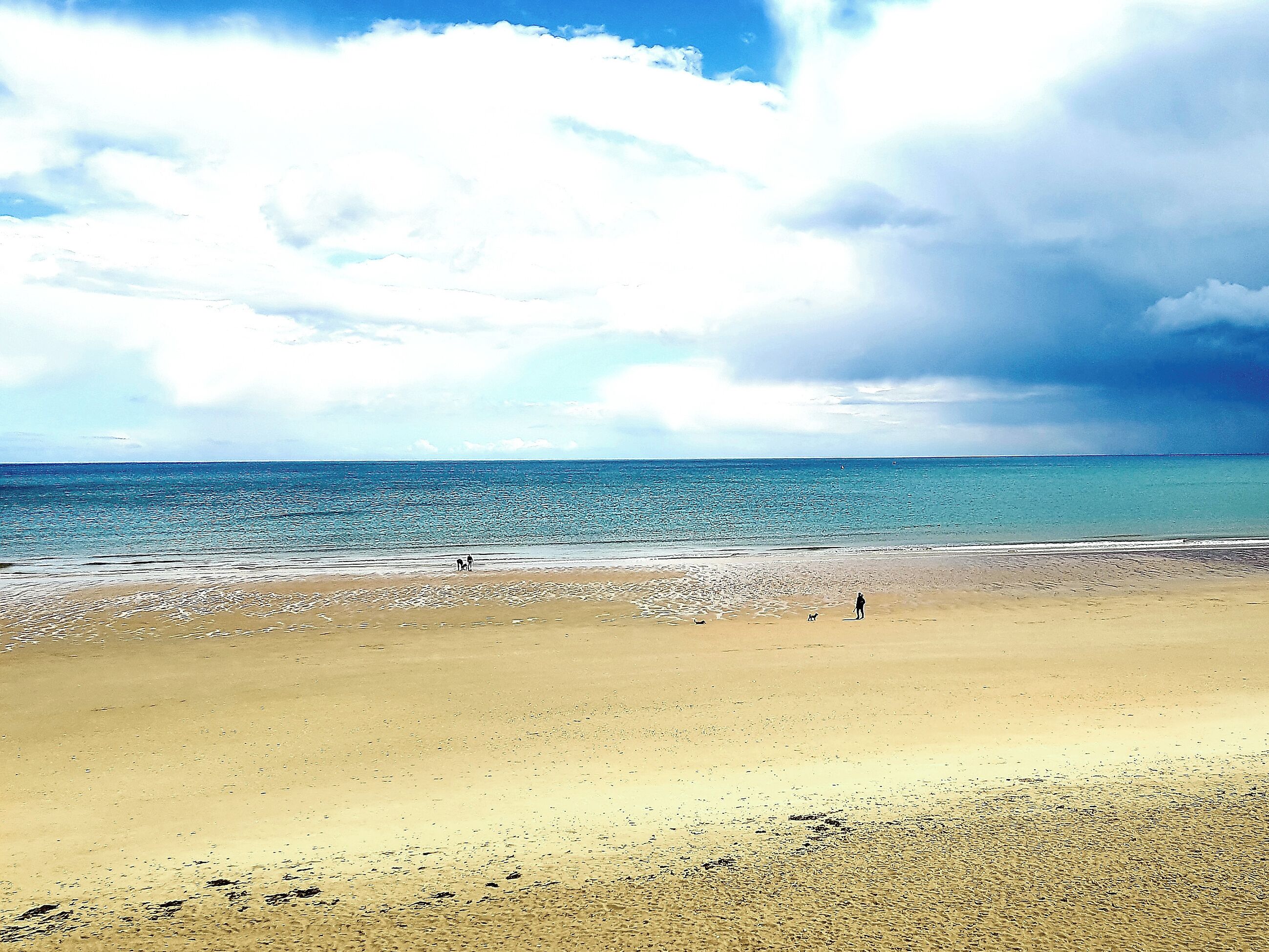 A beach with a wide sandy shore and a calm sea under a partly cloudy sky.