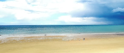 A beach with a wide sandy shore and a calm sea under a partly cloudy sky.