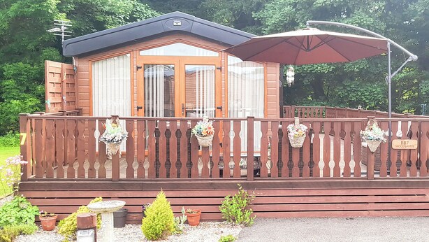 A wooden cabin with a balcony, a covered patio, and a gravel driveway. - Woodlands - Bridlington Links (Sewerby, near Bridlington)