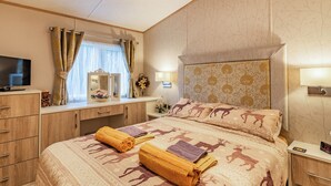 A hotel room with a bed, a TV, a dresser, and a nightstand with a clock. - Woodlands - Bridlington Links (Sewerby, near Bridlington)