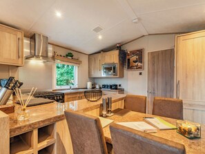 Een moderne keuken met houten kastjes, roestvrijstalen apparatuur en een eethoek met een marmeren aanrechtblad en stoelen.