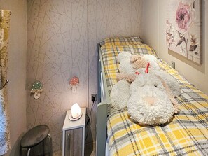 Een slaapkamer met een bed belegd met een geruite deken, een bedlampje, een klein krukje en een decoratief item aan de muur.