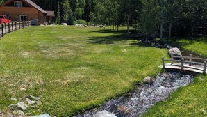 A grassy area with a small stream, a wooden bridge, and a cabin in the background. - House - 3 BR - 2 BA - Sleeps 10
 (Yampa)