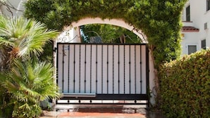 A gated entrance with a metal gate, surrounded by lush greenery and a tiled pathway. - Beverly Hills Celebrity Home (Los Angeles)