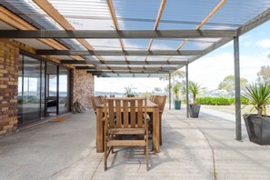 A covered patio area with a wooden table and chairs, a brick wall, and large windows.