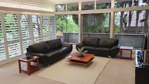 Uma sala de estar ampla com dois sofás de couro preto, uma mesa de centro de madeira e uma janela grande com vista para o verde.