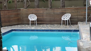 Piscina com duas cadeiras de plástico branco e um banco de madeira.