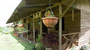 A wooden building with a porch, hanging flower pots, and potted plants. - Oski Lodge  (Guayabo)