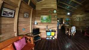 A cozy cabin interior with wooden walls, a wooden bench, a TV, and a small table with decorative items. - Oski Lodge  (Guayabo)