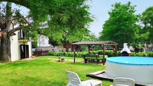 Ein Garten mit Schwimmbad, zwei weißen Plastikstühlen, einer Holzbank und einem Grill.