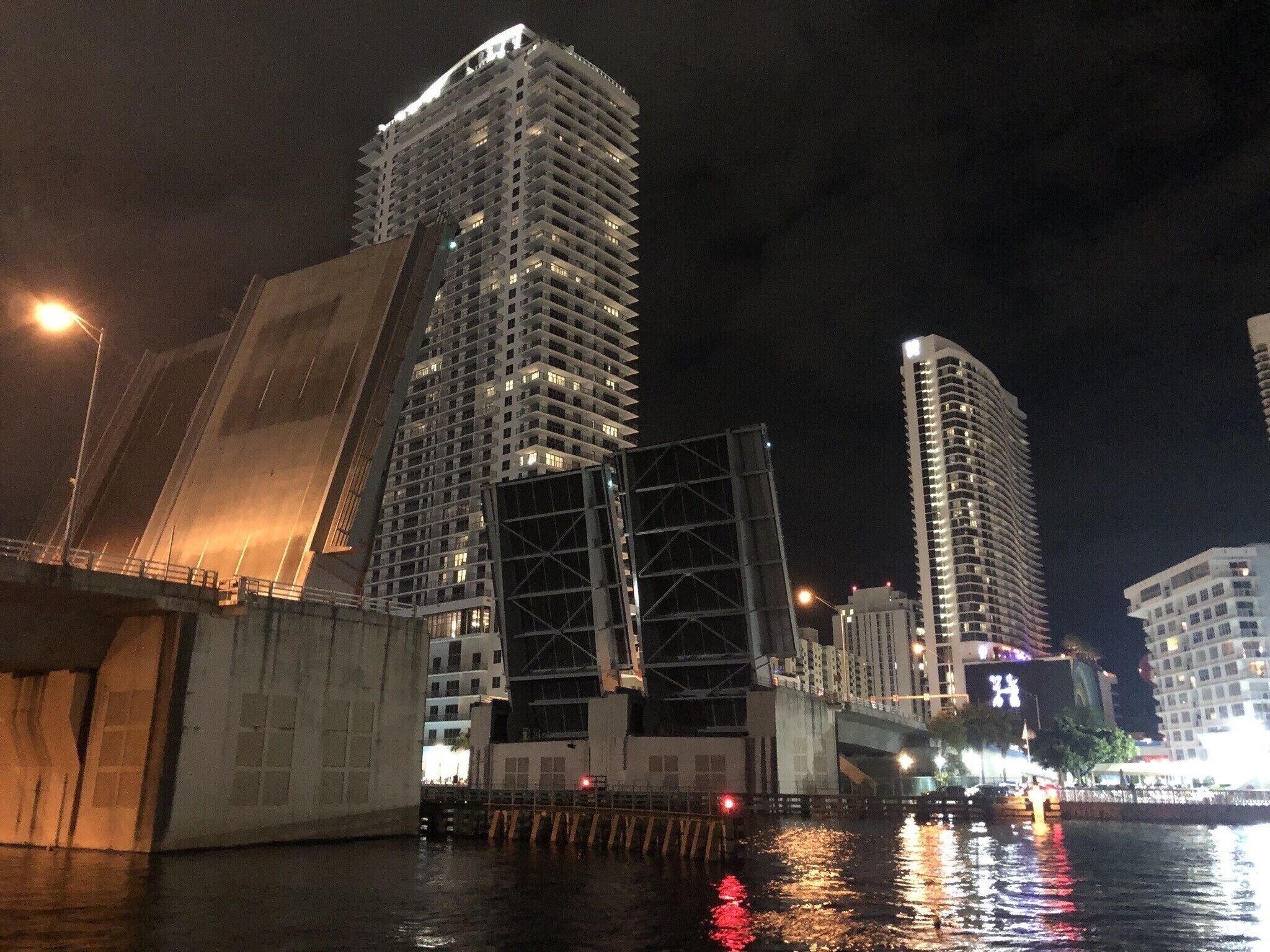 A nighttime cityscape with high-rise buildings, a bridge, and a waterfront.