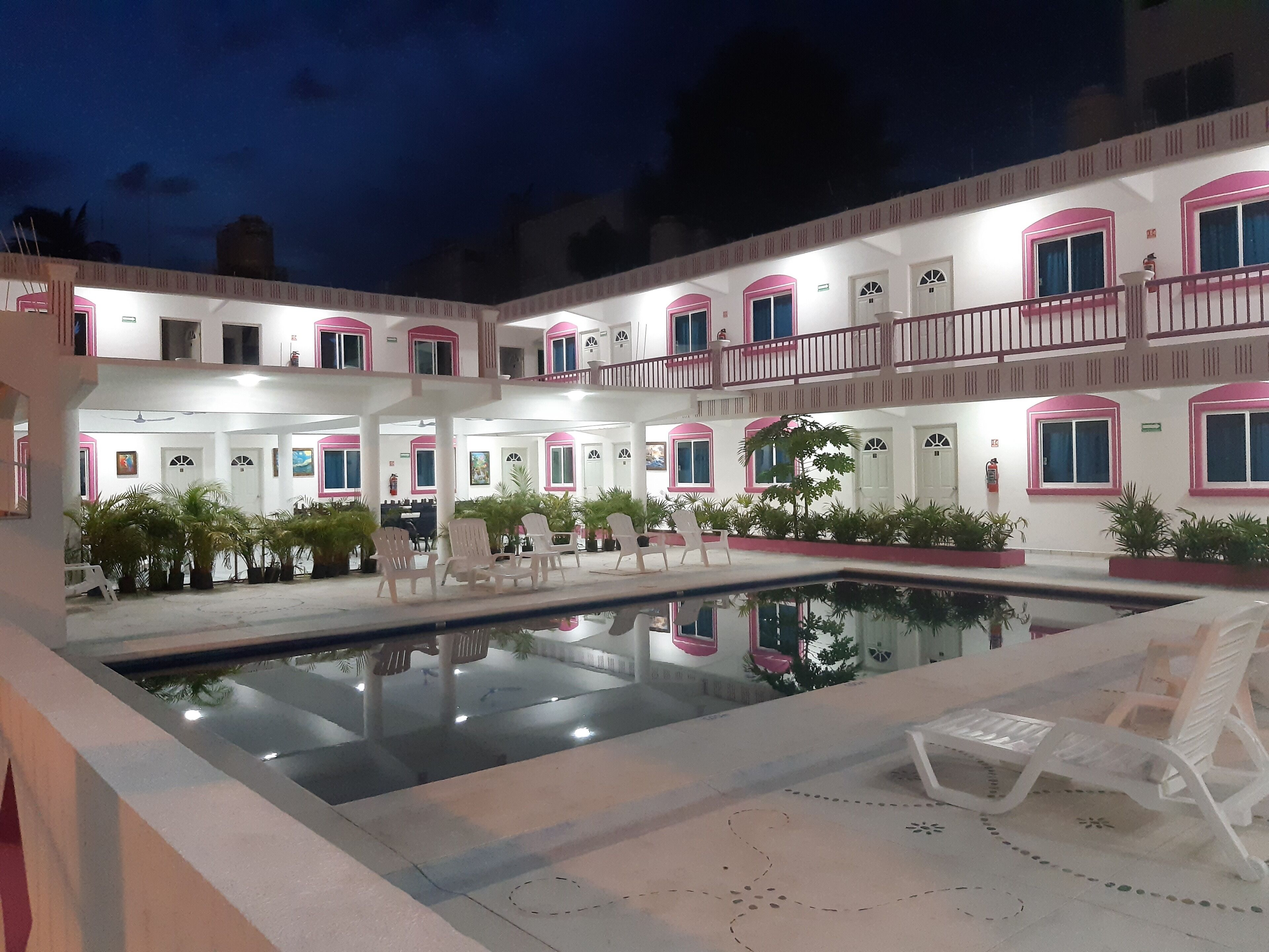 A multi-story hotel with a central courtyard featuring a swimming pool, outdoor seating, and potted plants.