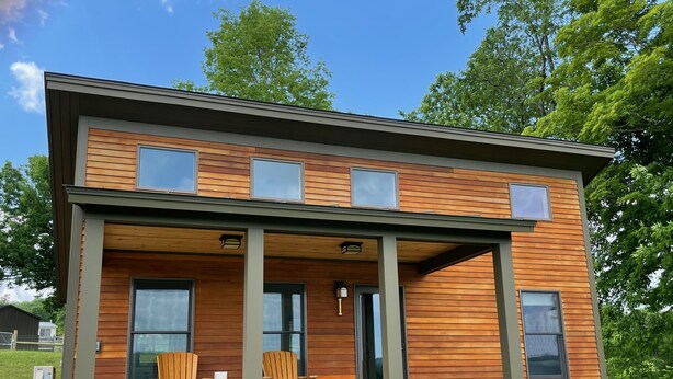 Un bâtiment moderne à deux étages, doté d’une façade en bois, de grandes fenêtres et d’un porche couvert avec des sièges.