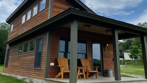 Une maison en bois à deux étages, dotée d’un porche couvert et de deux fauteuils Adirondack.