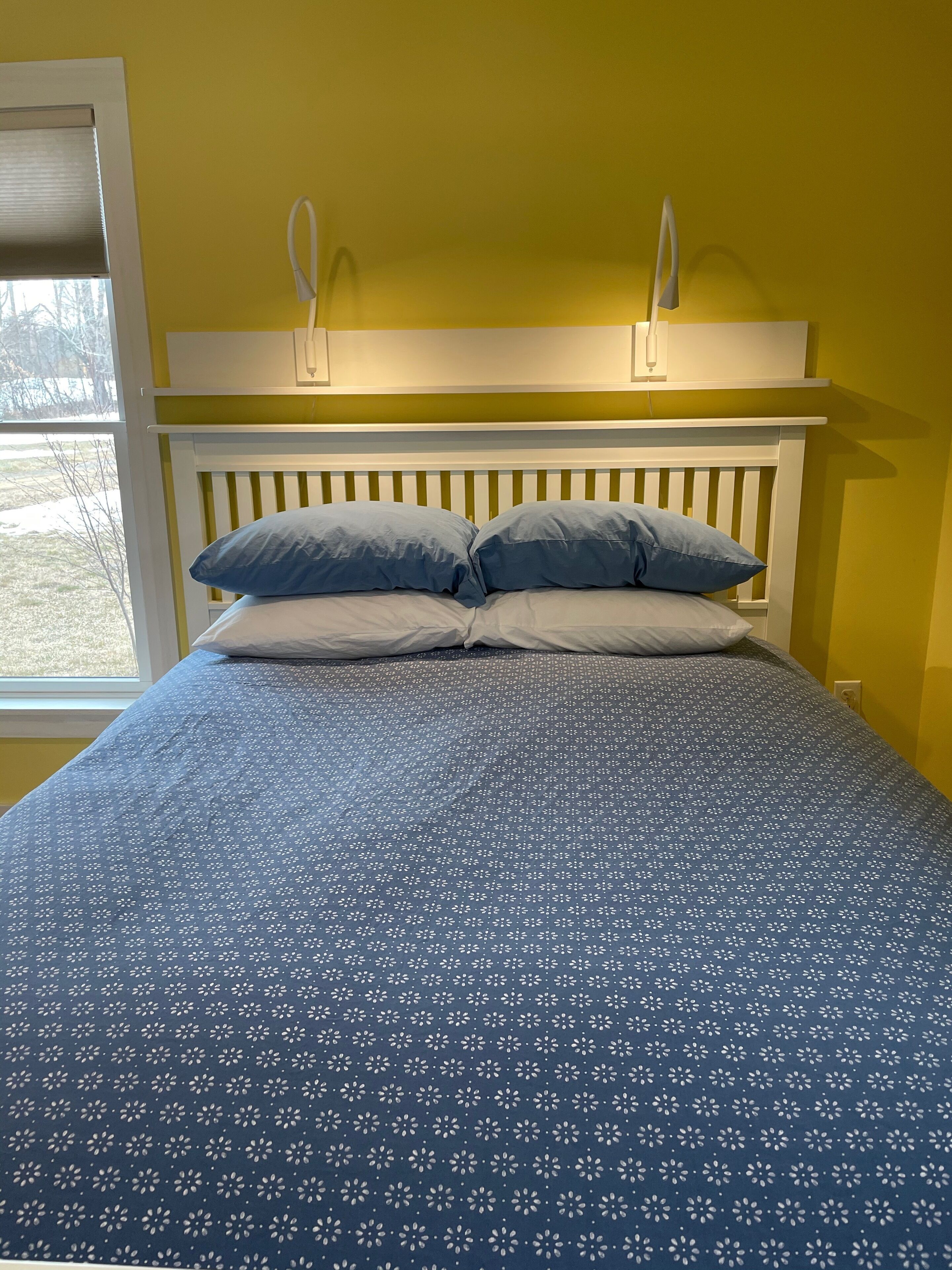 Una cama con una colcha azul estampada con flores, un cabecero blanco y dos almohadas.