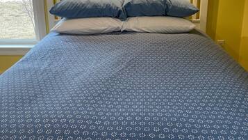 Una cama con una colcha azul estampada con flores, un cabecero blanco y dos almohadas.