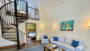 Un salon avec un escalier en colimaçon, un ensemble de canapés, une table basse et un tableau accroché au mur.