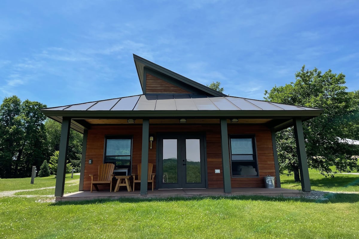 A modern house with a sloped roof, large windows, and a covered porch with chairs.