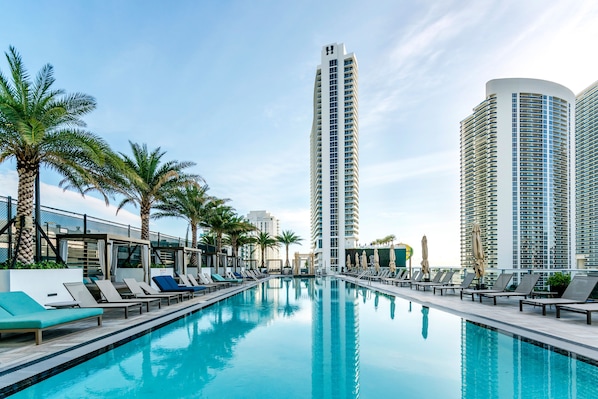 A swimming pool with lounge chairs and palm trees, surrounded by tall buildings.