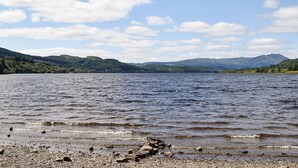 A lake with a rocky shoreline and distant mountains under a partly cloudy sky.