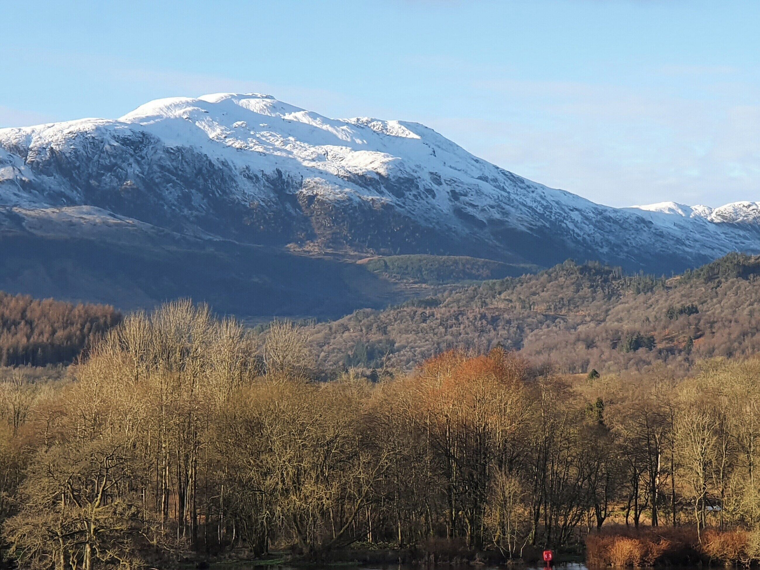 Paisagem de montanha com picos nevados e um vale arborizado.