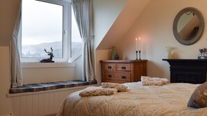 A bedroom with a large bed, a dresser, a mirror, and a window with a view of mountains.