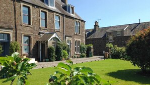 A stone house with a well-maintained lawn and a garden in the foreground.