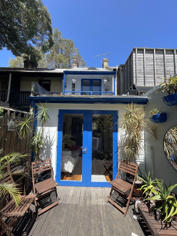 Una casa de dos pisos con puerta y ventanas azules, un muelle de madera y varias macetas con plantas.