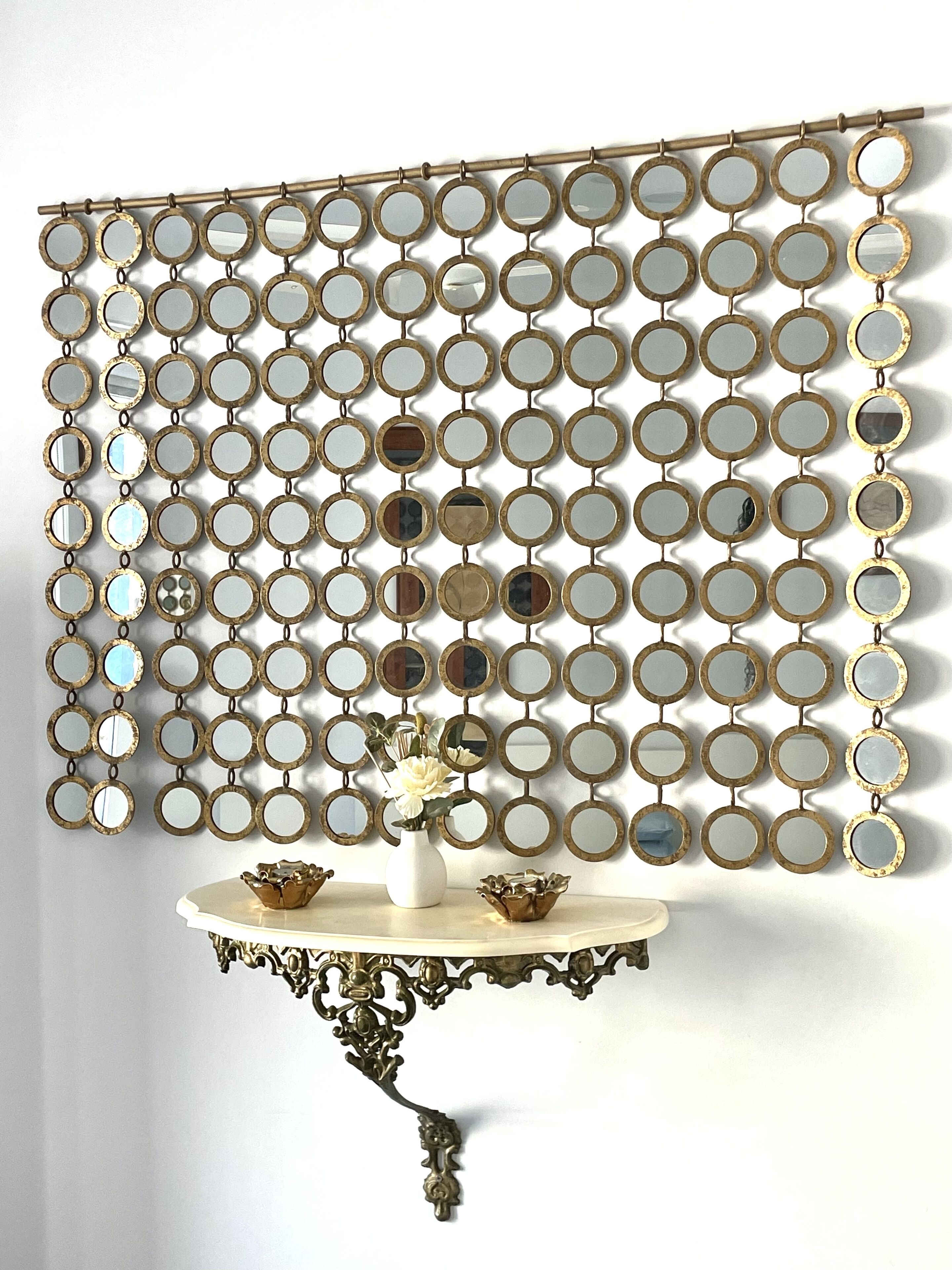 A wall with a decorative mirror arrangement and a small table with a vase and two bowls.