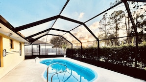 Piscina interior con techo de vidrio, rodeada por una terraza de concreto y vistas a una cerca de madera y árboles.