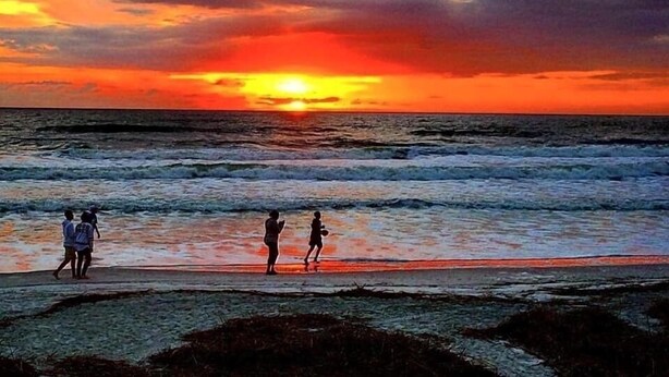 Un atardecer sobre el océano con gente caminando por la playa.