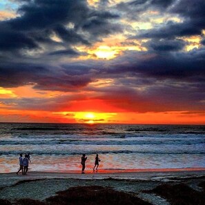 Un atardecer sobre el océano con gente caminando por la playa.