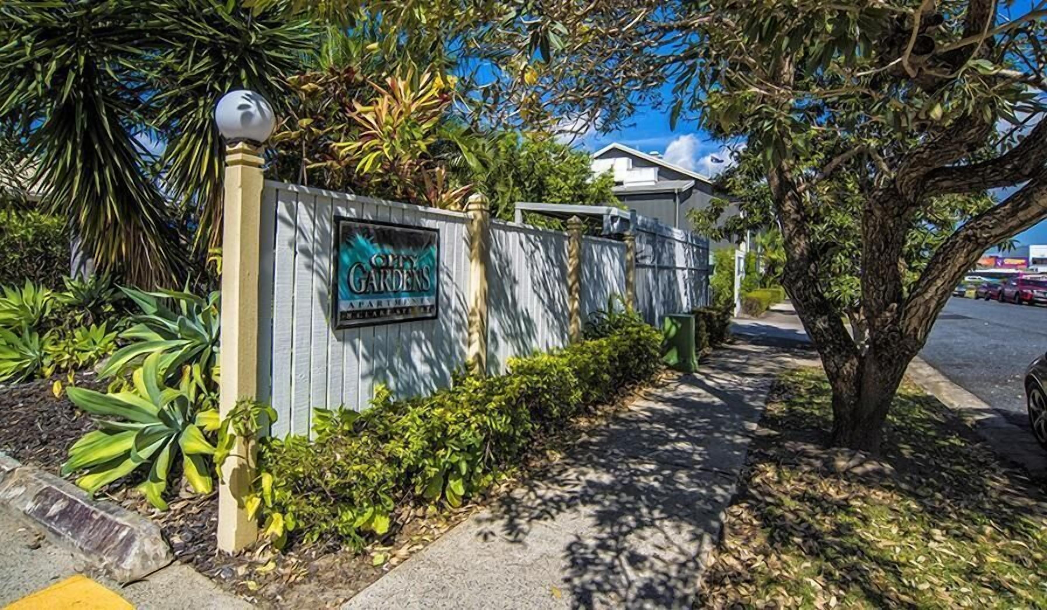 A gated entrance to a property named "City Gardens Apartments" with a sign, a pathway, and surrounding greenery.