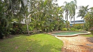 A landscaped garden with a swimming pool, surrounded by palm trees and a brick pathway. - Cairns City Garden Apartment (Parramatta Park)