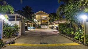 A hotel entrance with a covered parking area, palm trees, and a building with multiple floors and balconies. - Cairns City Garden Apartment (Parramatta Park)